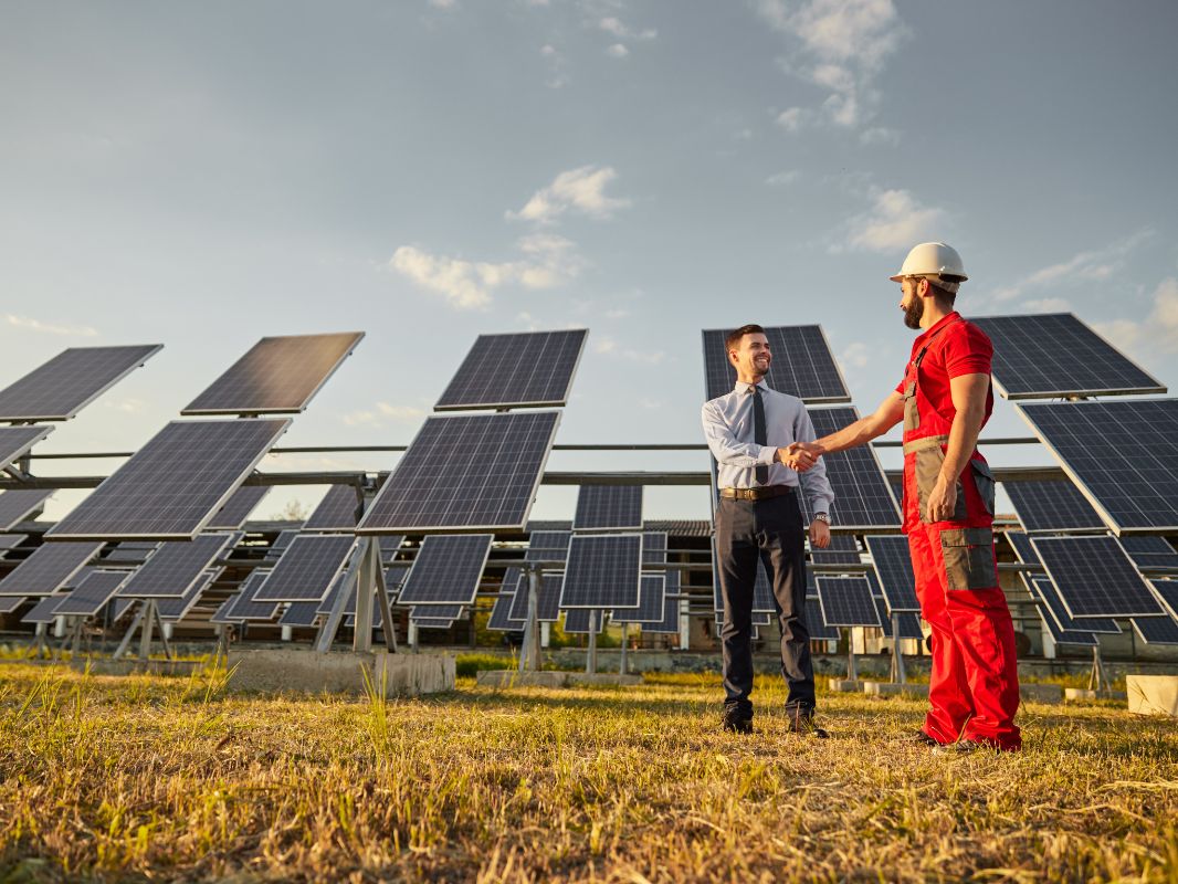 Ejecutivo estrechando manos con trabajador junto a paneles solares